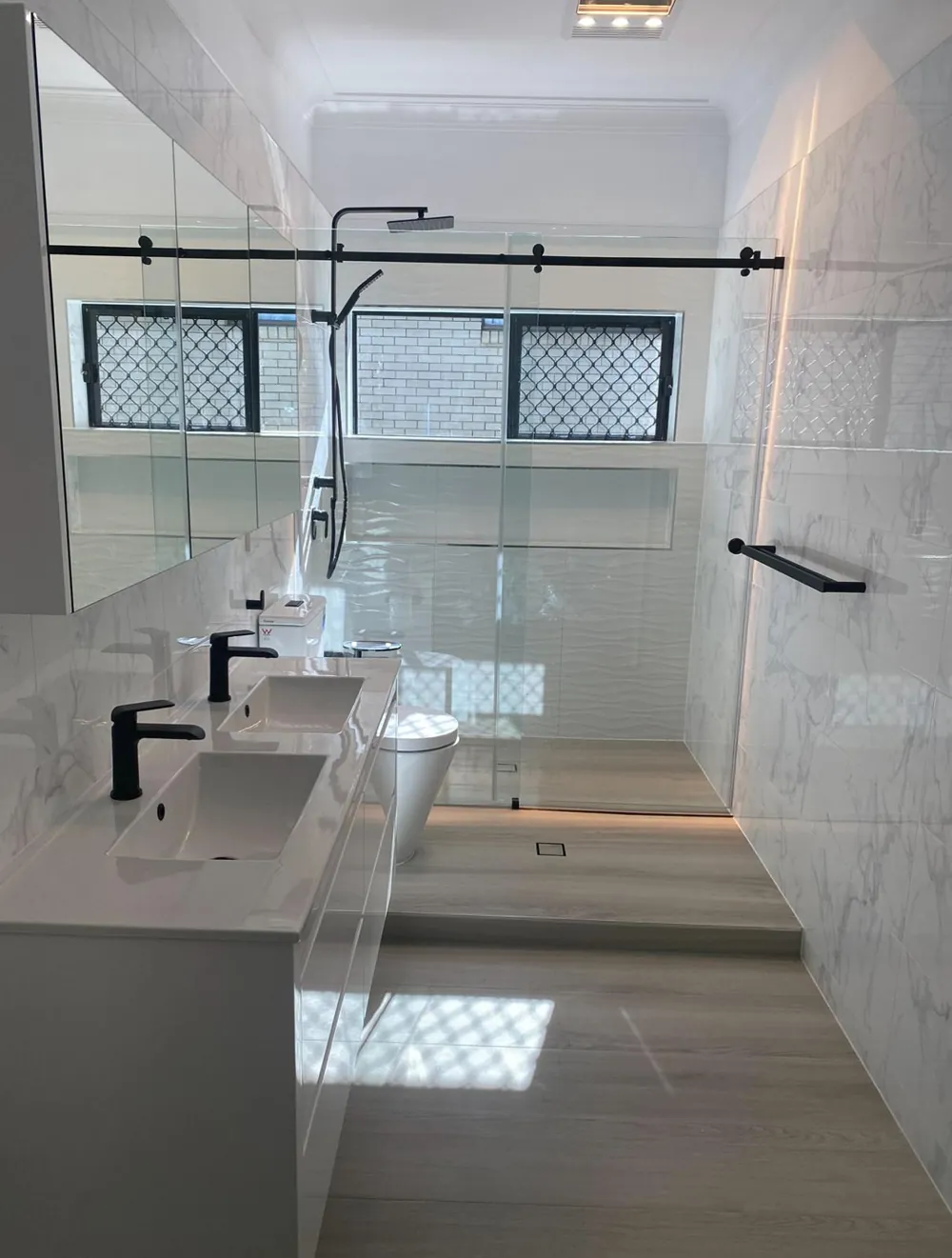 White marble-look bathroom with double vanity, black tapware and a glass shower screen